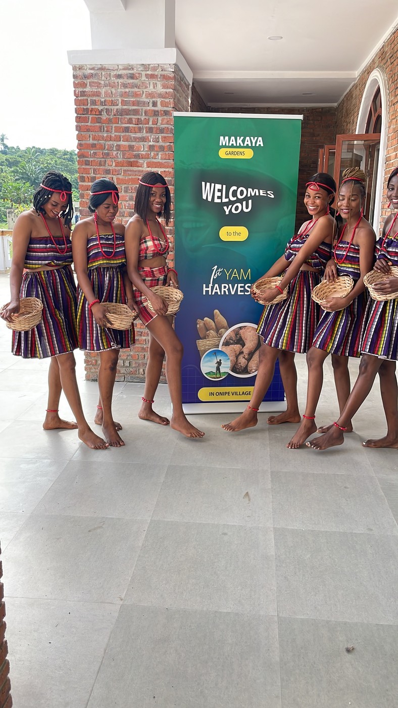 Dancers laughing together beside the 1st Yam Harvest banner at Onipe